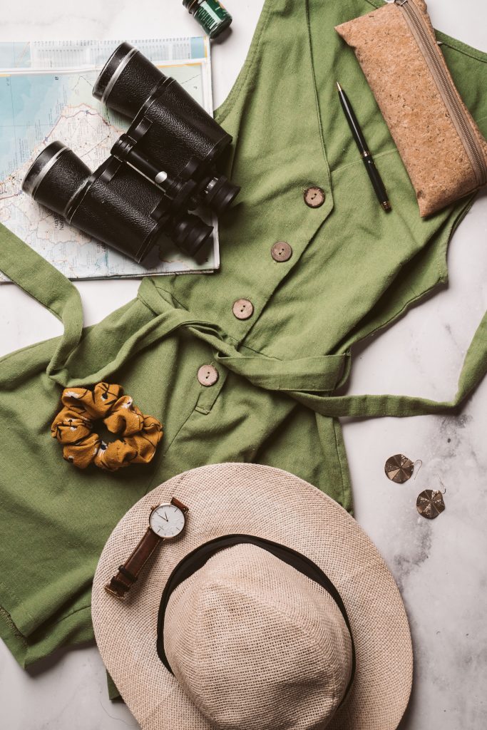 Flat lay of safari packing essentials - khaki clothing, binoculars, hat